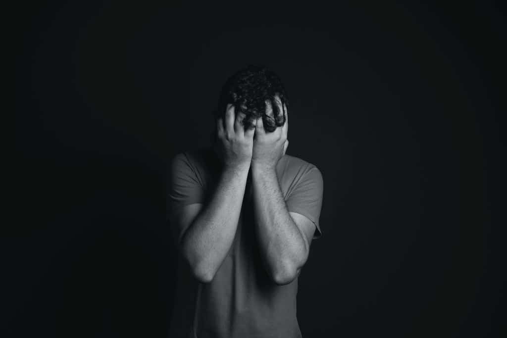 A greyscale shot of a man standing with his head in his hands - Which Rehab