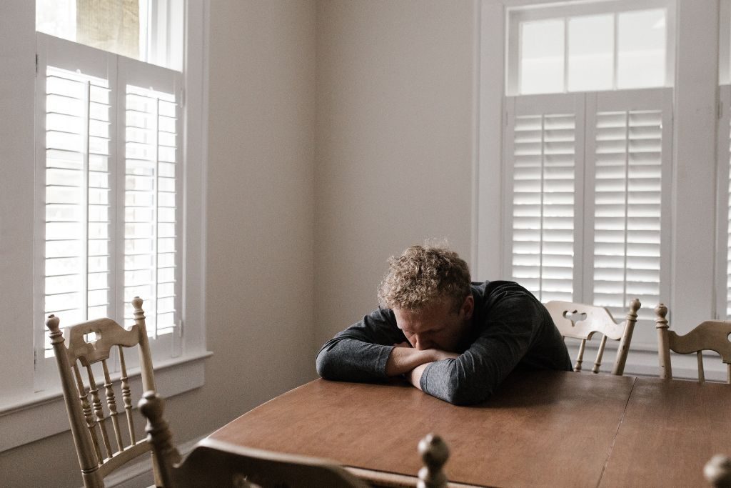 Man with head in arms leaning against a table - Which Rehab